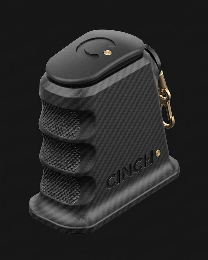 Cinch Loader, Glock fit. Black carbon fiber nylon magazine loader in three-quarter view on a dark ground, three finger scallops on the edge, CINCH debossed on the side, a brass swivel clip at the top.
