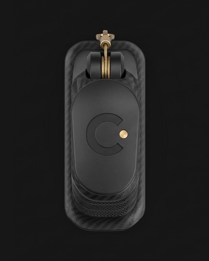 Cinch Loader, Taurus GX fit. Black carbon fiber nylon magazine loader seen from above on a dark ground, the C mark and a brass dot on the cap, a brass cord running from the tether reel to a swivel clip.
